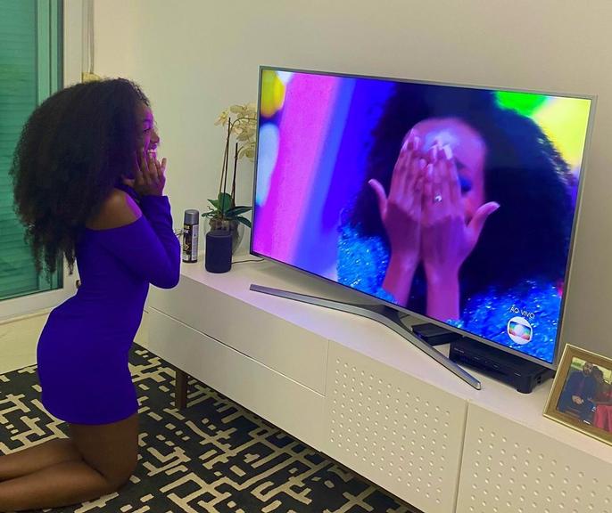 Ao assistir o anúncio da vitória de Thelma, Iza surge ajoelhada em frente à televisão 