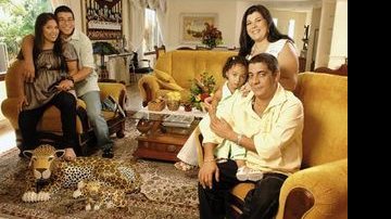 A família, menos o filho mais velho, posa na sala de estar com móveis de cores e formatos fortes e tapeçaria da santa ceia.