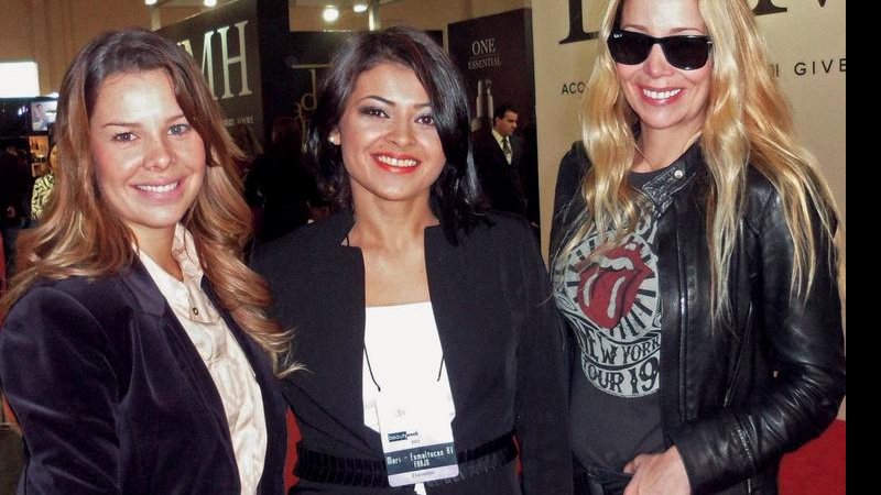 Em SP, Fernanda Souza e Danielle Winits ladeiam a maquiadora Marinalva Gomes em feira de cosméticos, em SP.