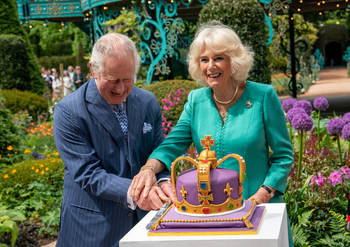 Charles e Camilla não conseguiram esconder os sorrisos quando se depararam com um bolo colorido e em formato de coroa. Quem cortou o bolo e se divertiu com a situação foi o Rei